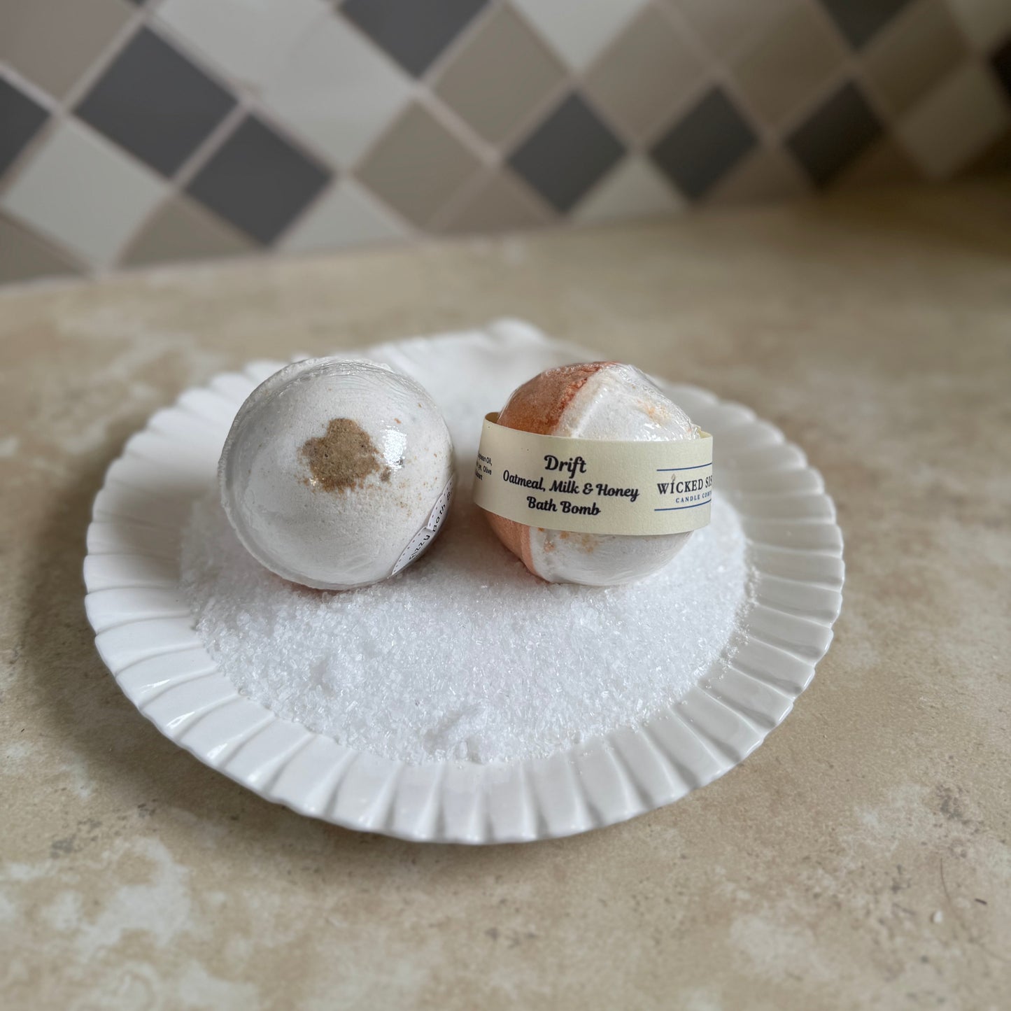 Two bath bombs on a white shell plate with a tiled wall background