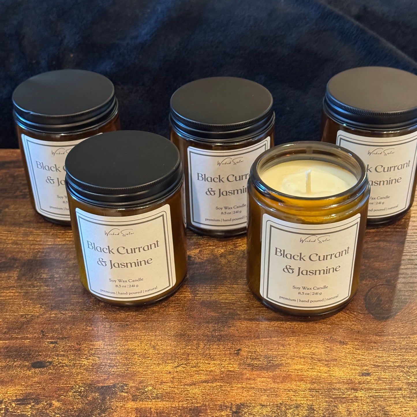 Jars of Black Current & Jasmine candles on a wooden surface