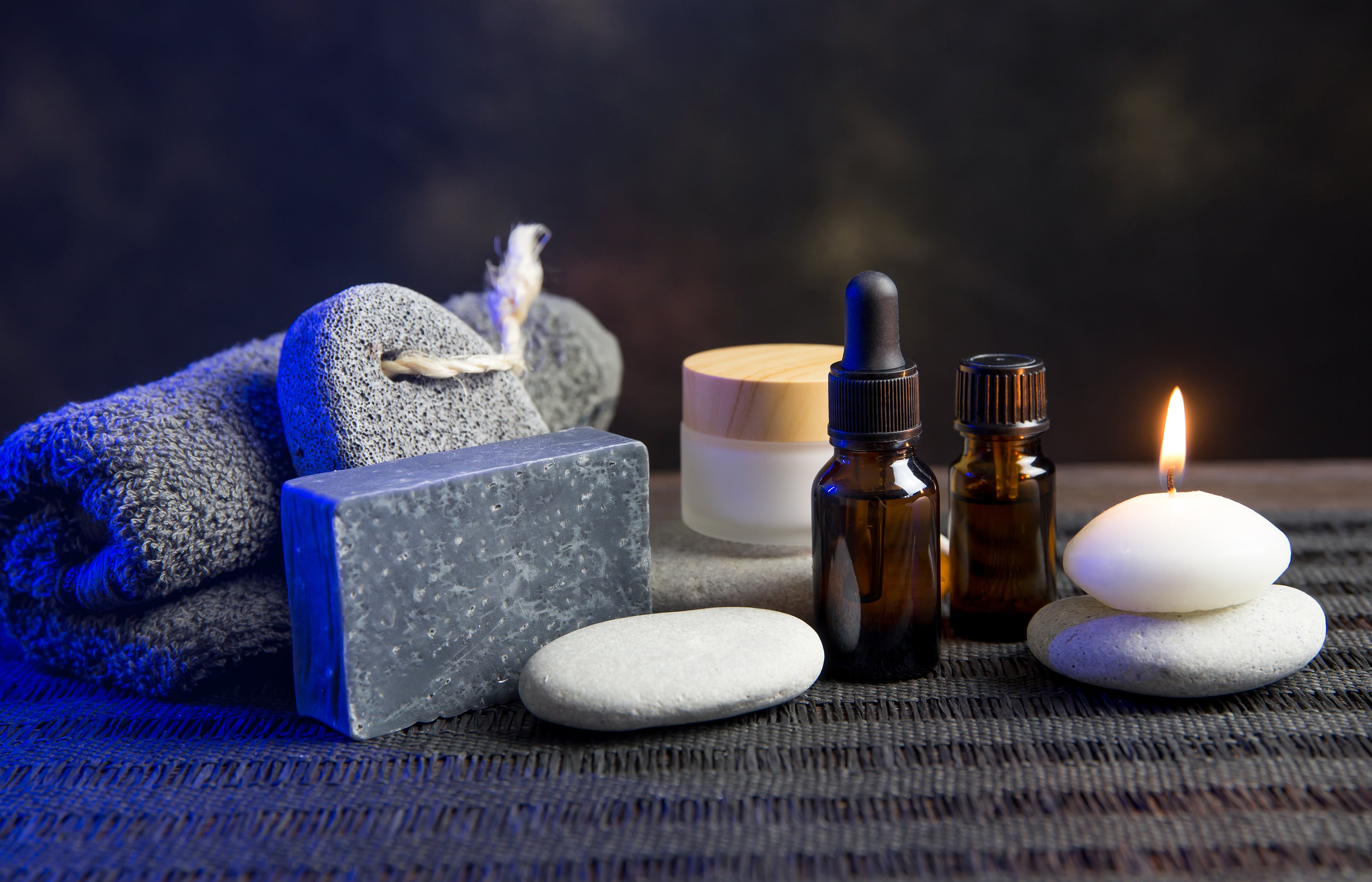 Aromatherapy setup with essential oils, candles, and towels on a dark background