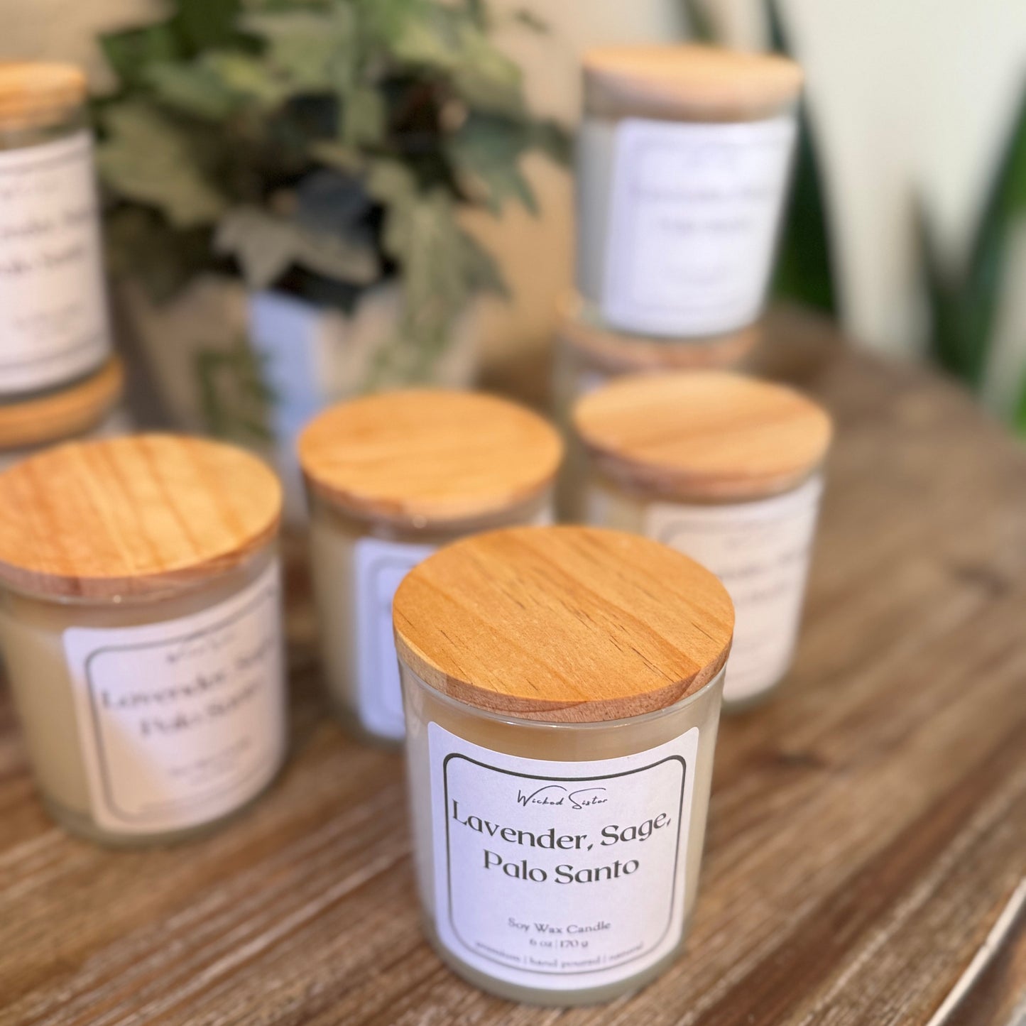 Set of candles with wooden lids on a wooden surface with plants in the background