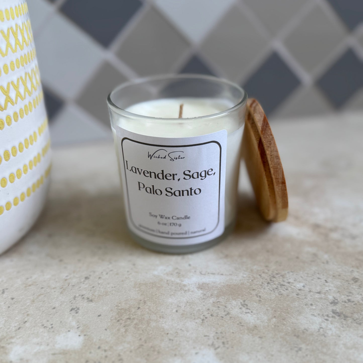Candle labeled 'Lavender, Sage, Palo Santo' on a countertop with a tiled wall background
