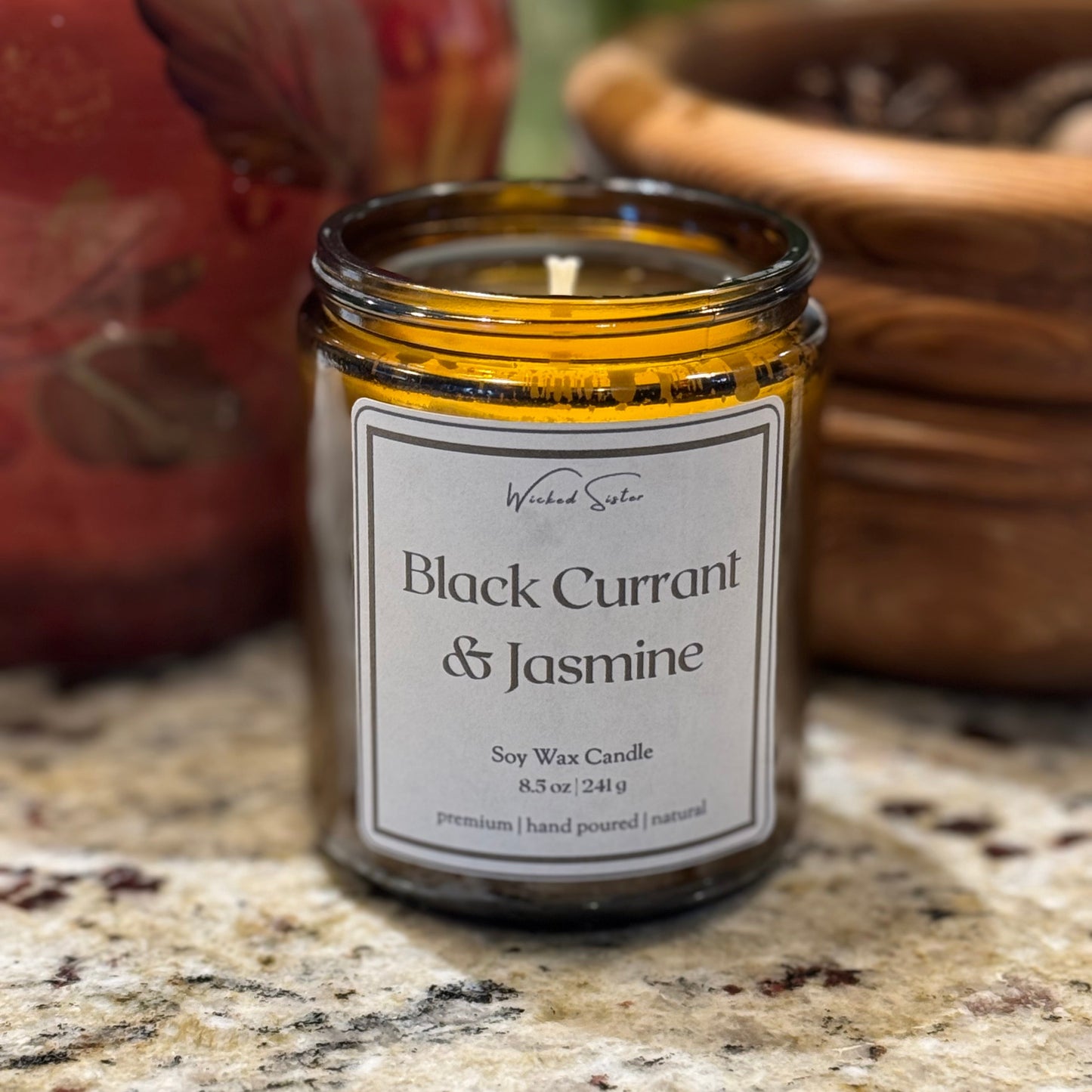 Candle labeled 'Black Currant & Jasmine' on a granite surface with a blurred background