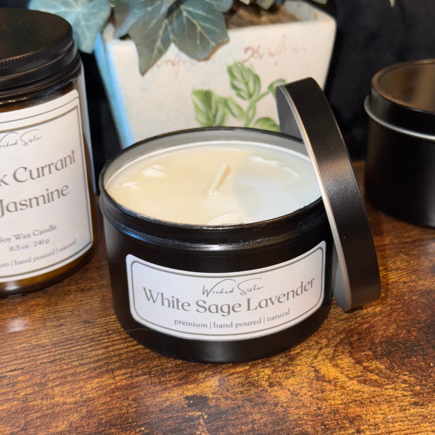 Candle tins with labels on a wooden surface next to a plant