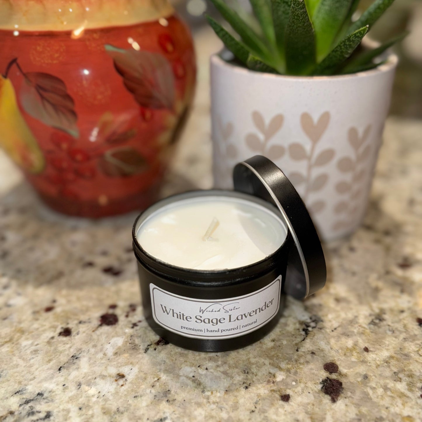 Candle labeled 'White Sage Lavender' on a granite surface with a potted plant and decorative item in the background.