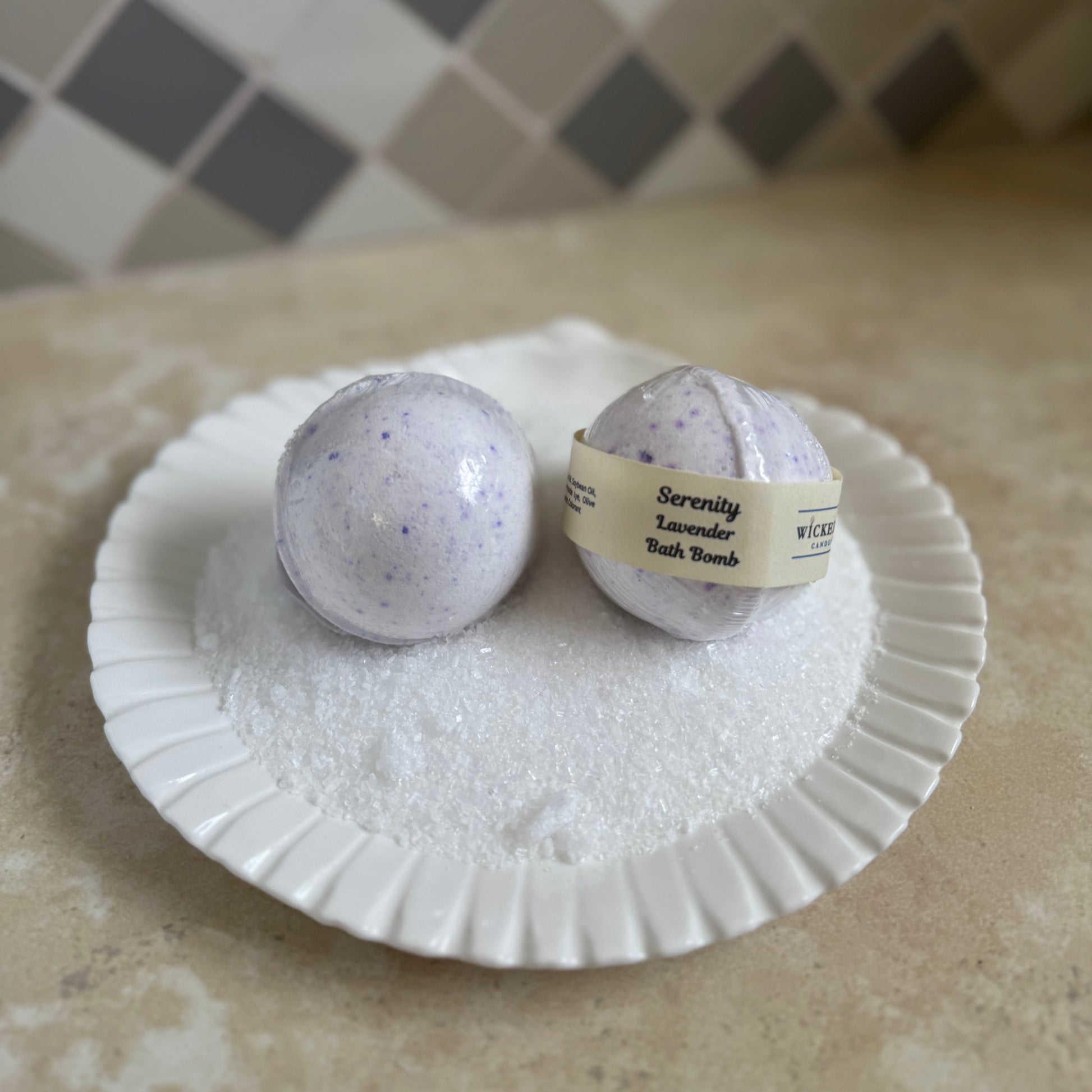Two lavender bath bombs on a white seashell plate with a checkered tile background