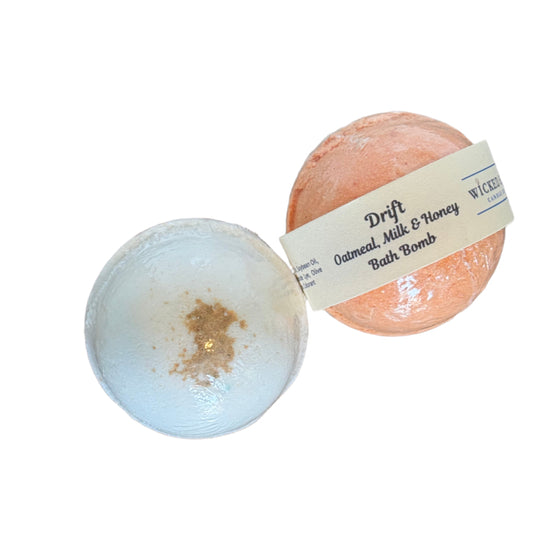 Two oat milk bath bombs, one tan and one white, on a clean white surface with a visible brand label.