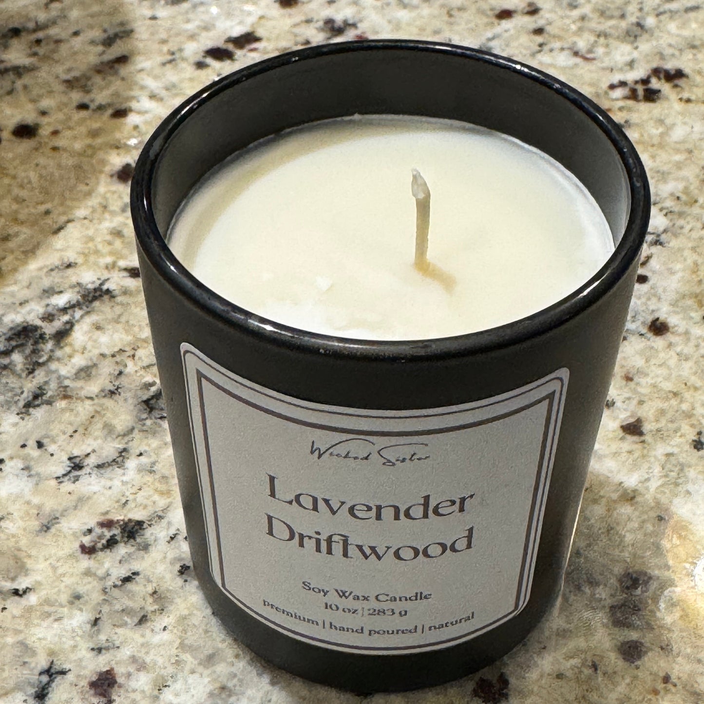 Candle in a black container labeled 'Lavender Driftwood' on a granite surface