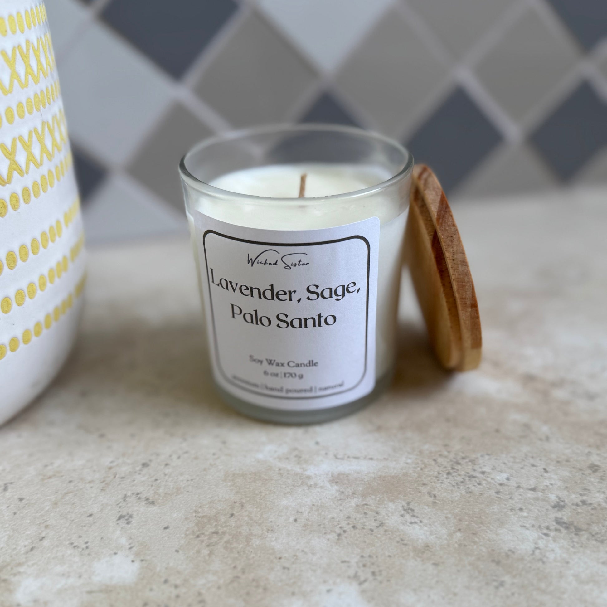 Candle labeled 'Lavender, Sage, Palo Santo' on a countertop with a tiled wall background