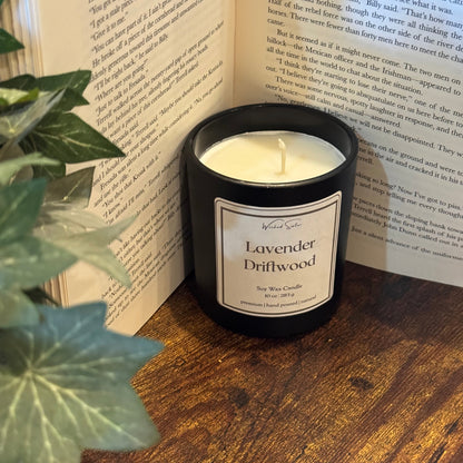 Candle labeled 'Lavender Driftwood' on an open book with a plant in the foreground.